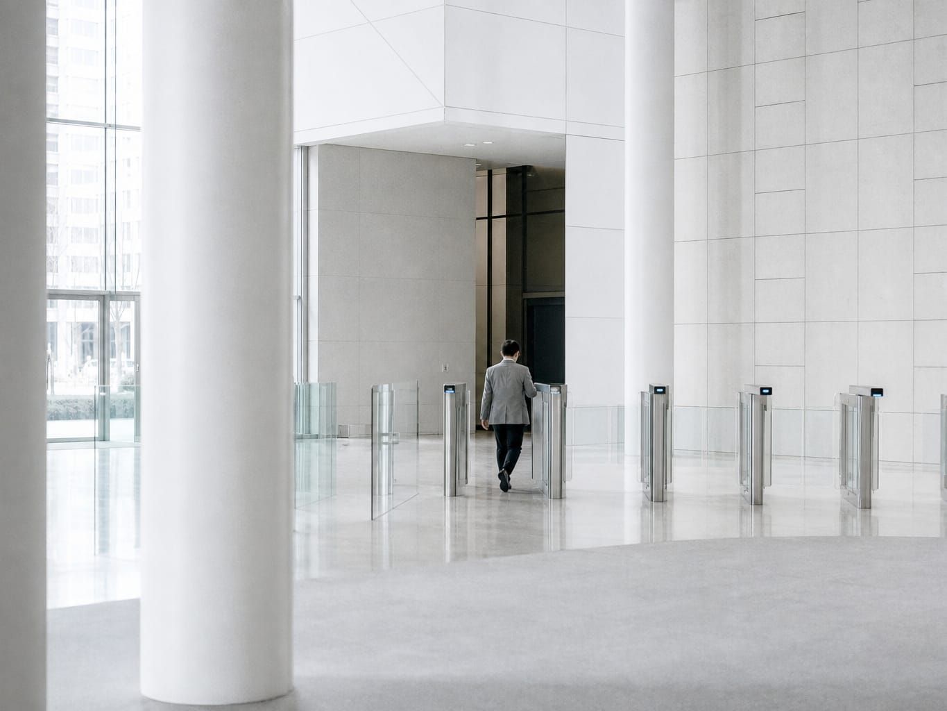 Vestíbulo blanco con columnas y tornos de cristal; una persona cruza uno de los tornos